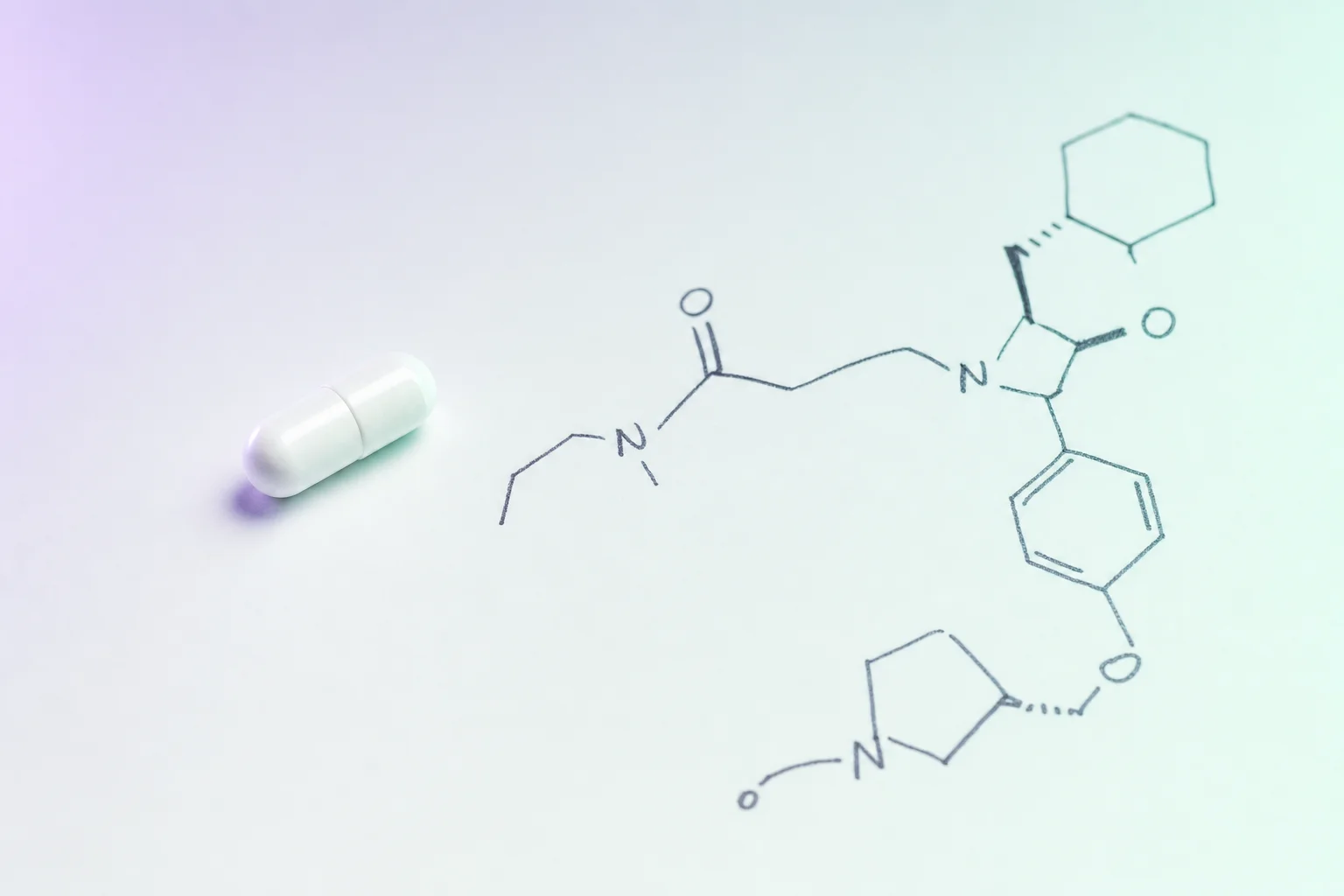 A small white capsule beside hand-drawn molecular notes on a near-white surface with cool lavender light