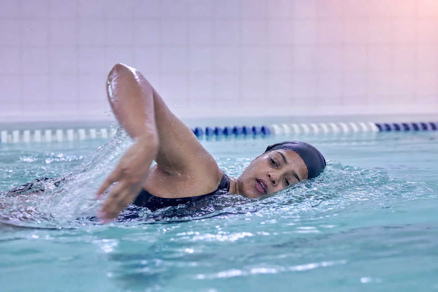 A woman in her fifties swimming laps in an indoor pool, caught mid-stroke turning to breathe