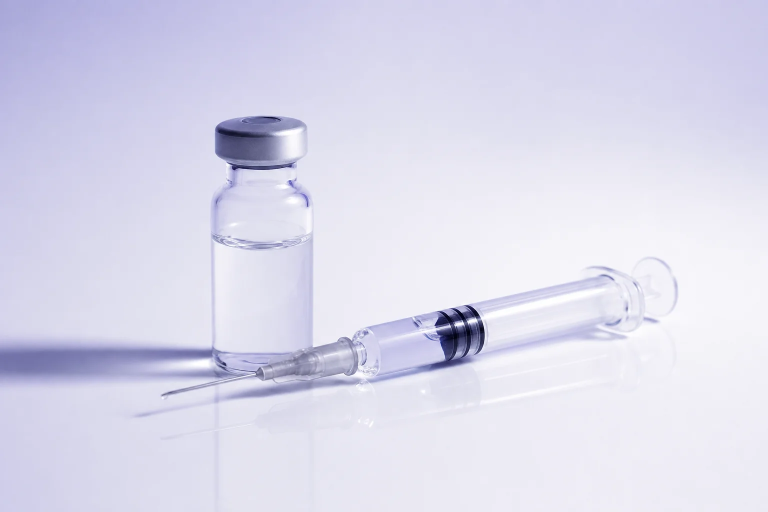 A pre-filled syringe beside a glass vial on a near-white surface — evoking the choice between direct hormone replacement and natural stimulation